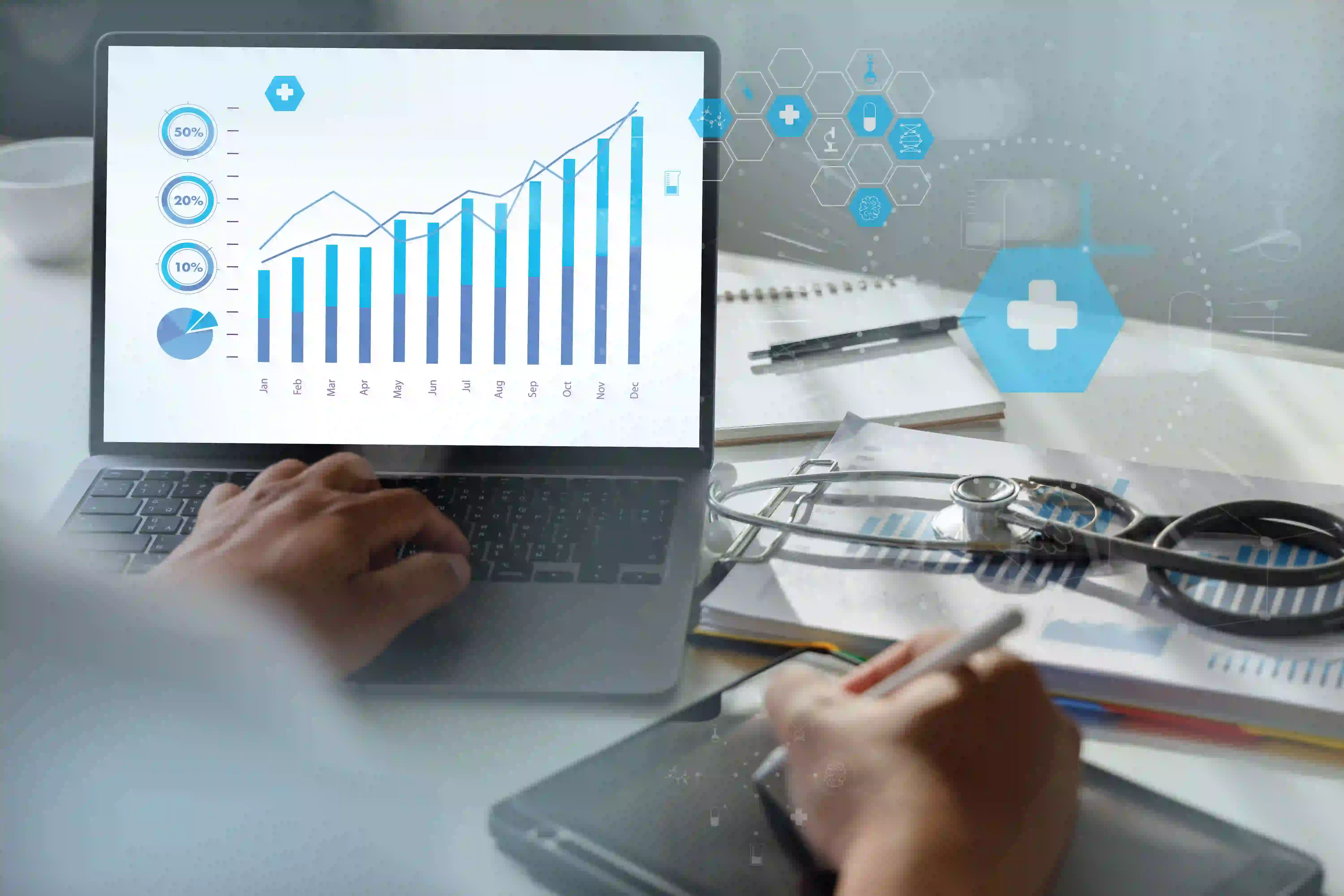 Hospital finance staff reviewing monthly revenue charts on a laptop beside a stethoscope and printed billing reports